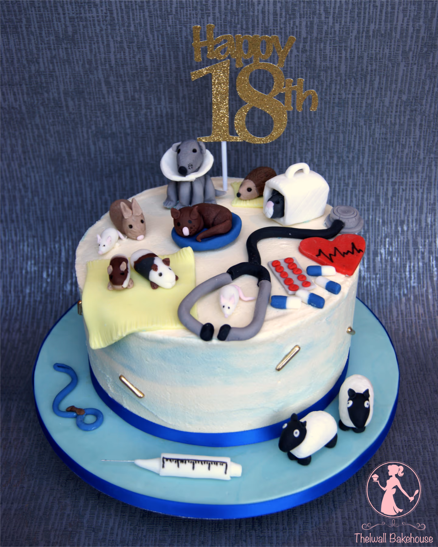 An 18th birthday cake with a veterinary theme, featuring fondant animals such as a dog with a cone, a sleeping dog, a rabbit, a hedgehog, guinea pigs, mice, and two sheep. It is also decorated with medical items like a stethoscope, pills, a syringe, and a heart monitor graph, topped with a gold glitter 'Happy 18th' sign.