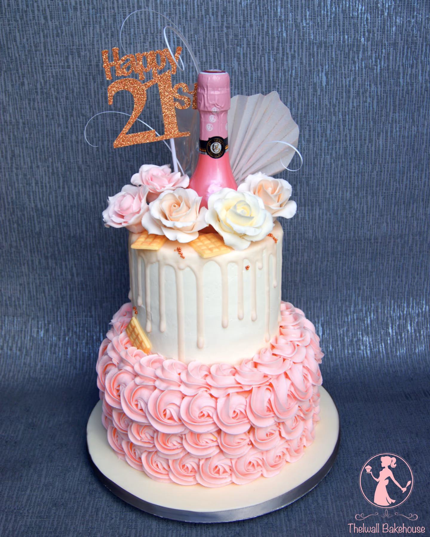 Two-tier 21st birthday cake featuring a white top tier with pink drip icing, decorated with a miniature pink champagne bottle, a 'Happy 21st' glitter topper, and an assortment of pink, cream, and white sugar roses, while the bottom tier is covered in pink rosette buttercream piping.