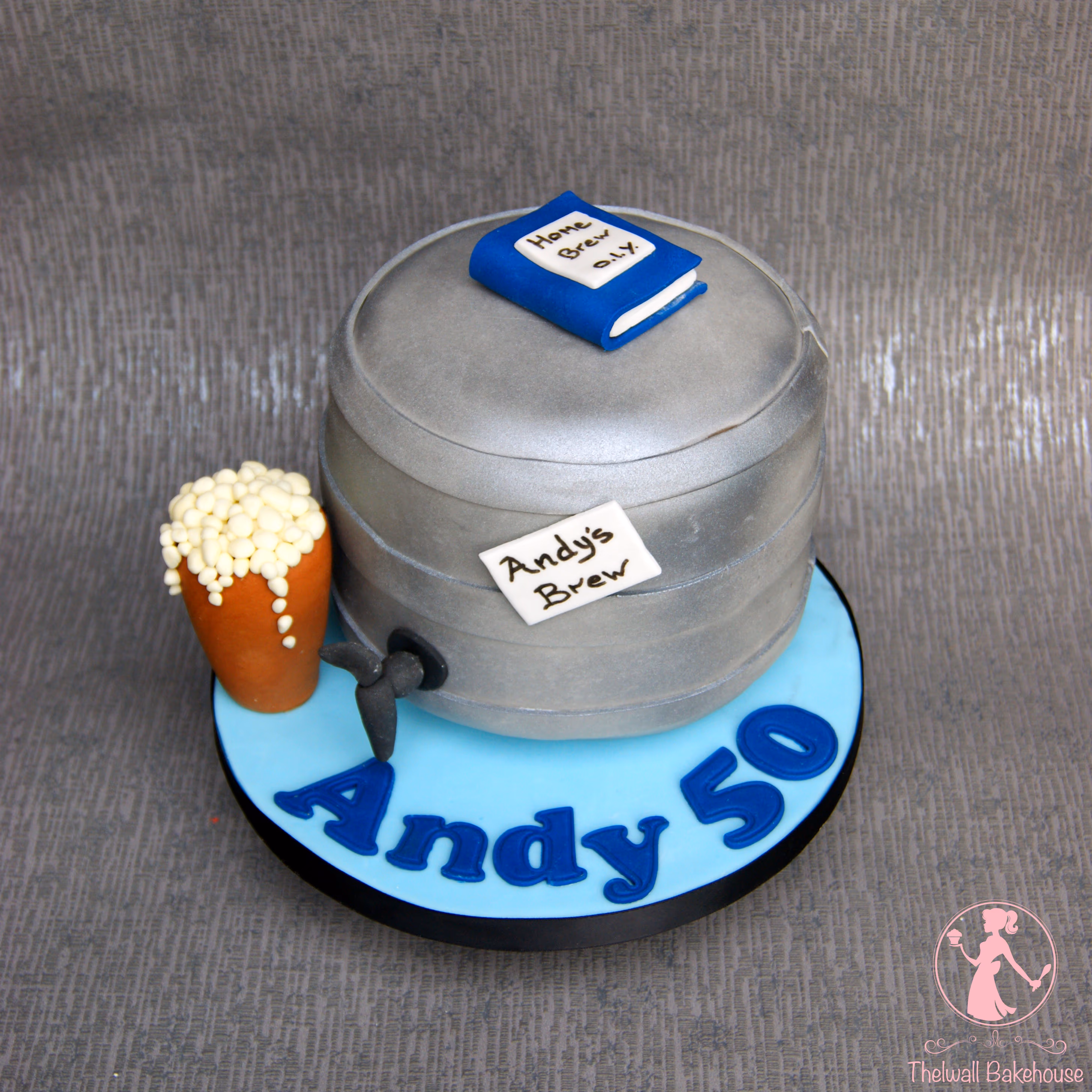 A men's 50th birthday cake shaped like a silver beer keg, with a blue 'Home Brew O.I.Y.' book on top, an 'Andy's Brew' label, a black tap, and a separate small beer glass with white foam, all on a light blue base with 'Andy 50' in dark blue letters.