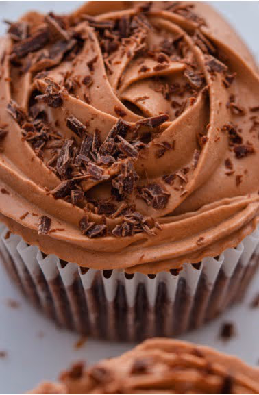 A close-up of a chocolate cupcake with swirled chocolate frosting and chocolate shavings.