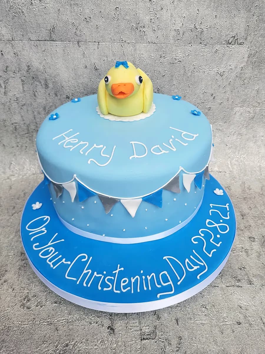 Two-tier blue christening cake with duck topper and bunting