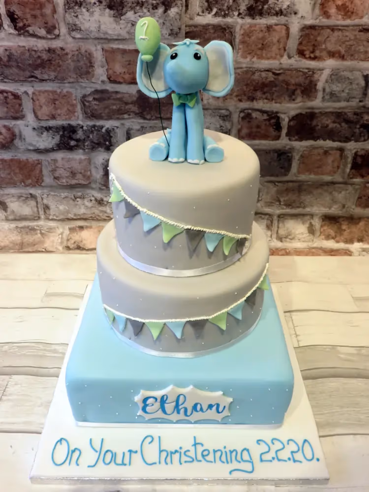 Two-tier blue and grey christening cake with elephant and bunting