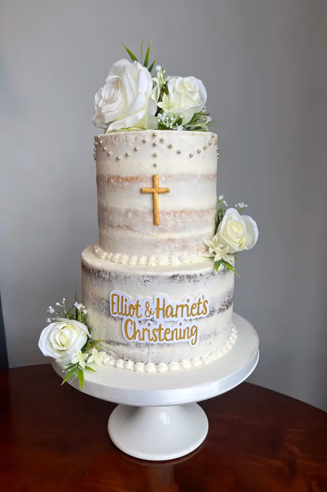 Two-tier naked christening cake with white flowers and gold cross