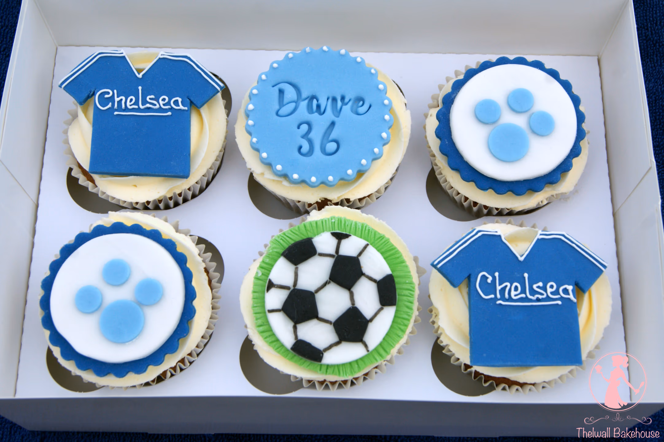 Six football-themed cupcakes in a white box, featuring two blue Chelsea FC shirts, two blue and white paw prints, one football, and one blue cupcake with "Dave 36" written on it.
