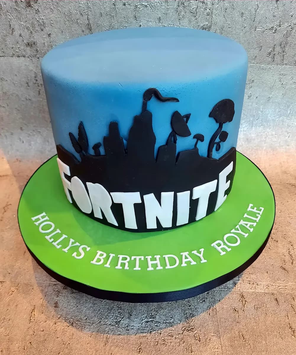 A round, single-tier Fortnite-themed birthday cake. The cake has a light blue top and a black silhouette design of Fortnite landscape elements around its side, with the word 'FORTNITE' in bold white letters. The cake sits on a bright green board, which has 'HOLLYS BIRTHDAY ROYALE' written in white fondant letters around its edge.