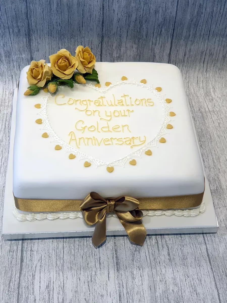 Square golden anniversary cake with white fondant, gold roses and ribbon