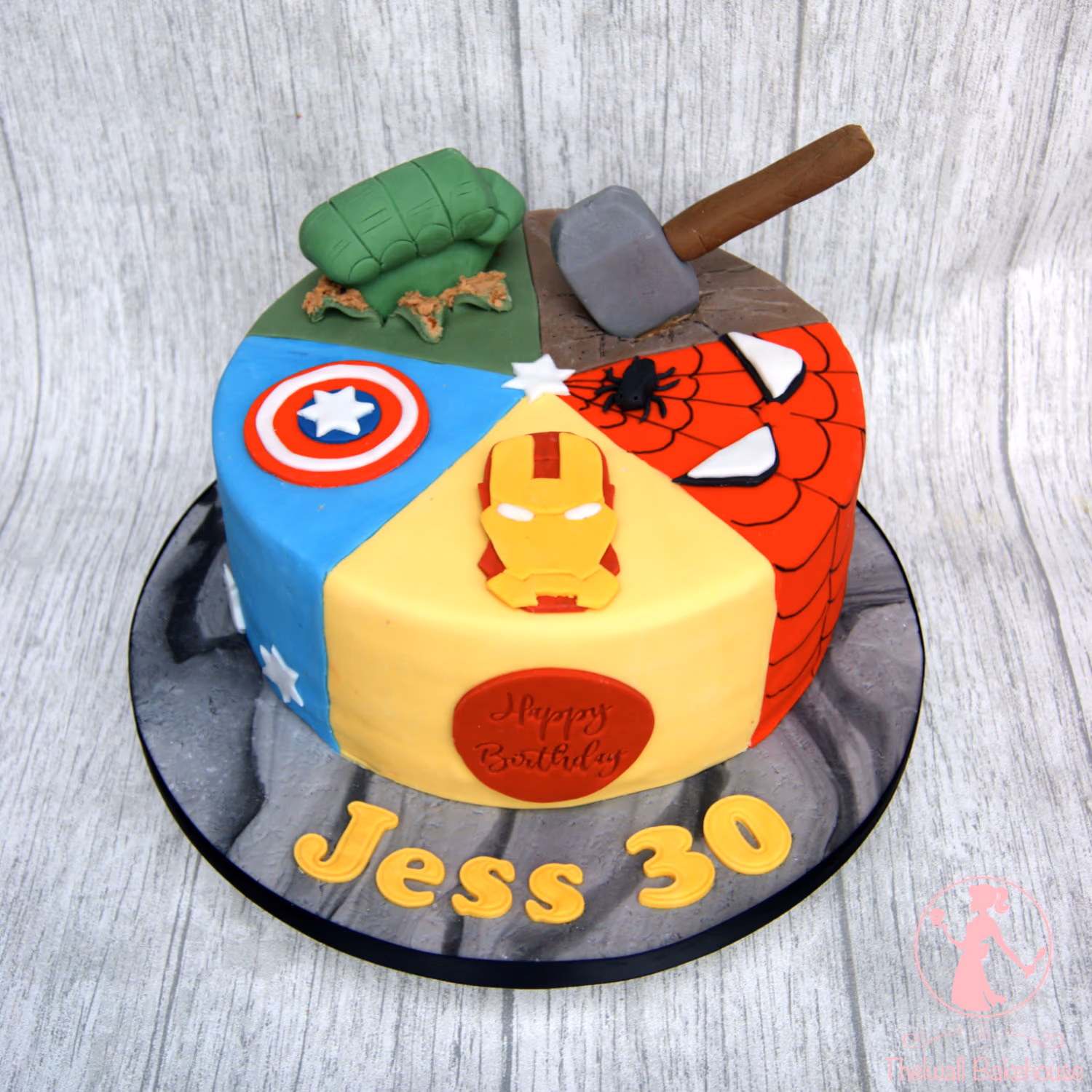 Round birthday cake decorated with four Marvel superhero themes: Hulk, Thor, Spider-Man, and Captain America, featuring an Iron Man mask on the front and 'Happy Birthday Jess 30' on the cake board.