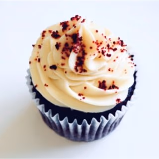 A single red velvet cupcake topped with a swirl of light cream frosting and red crumbs.