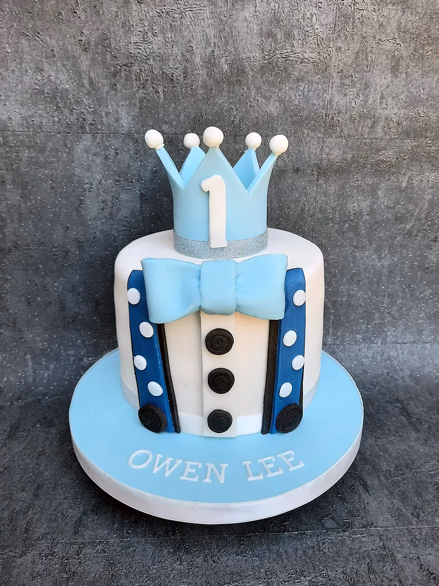 Boy's 1st birthday cake in blue and white with crown, suspenders, and bow tie
