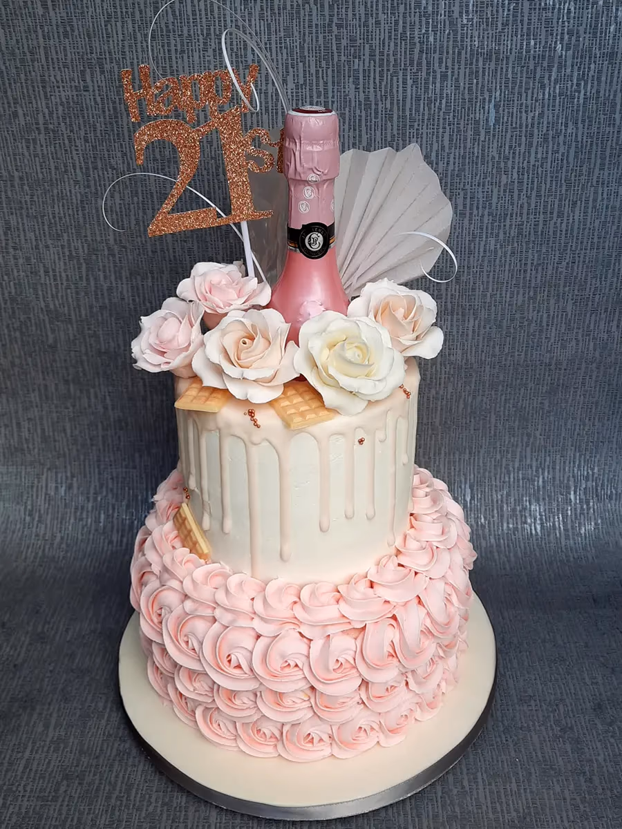 Two-tier 21st birthday cake with pink rosettes, white drip, and champagne decoration