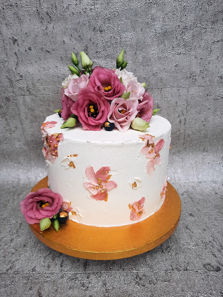 White celebration cake with pink and fuchsia flowers and gold leaf