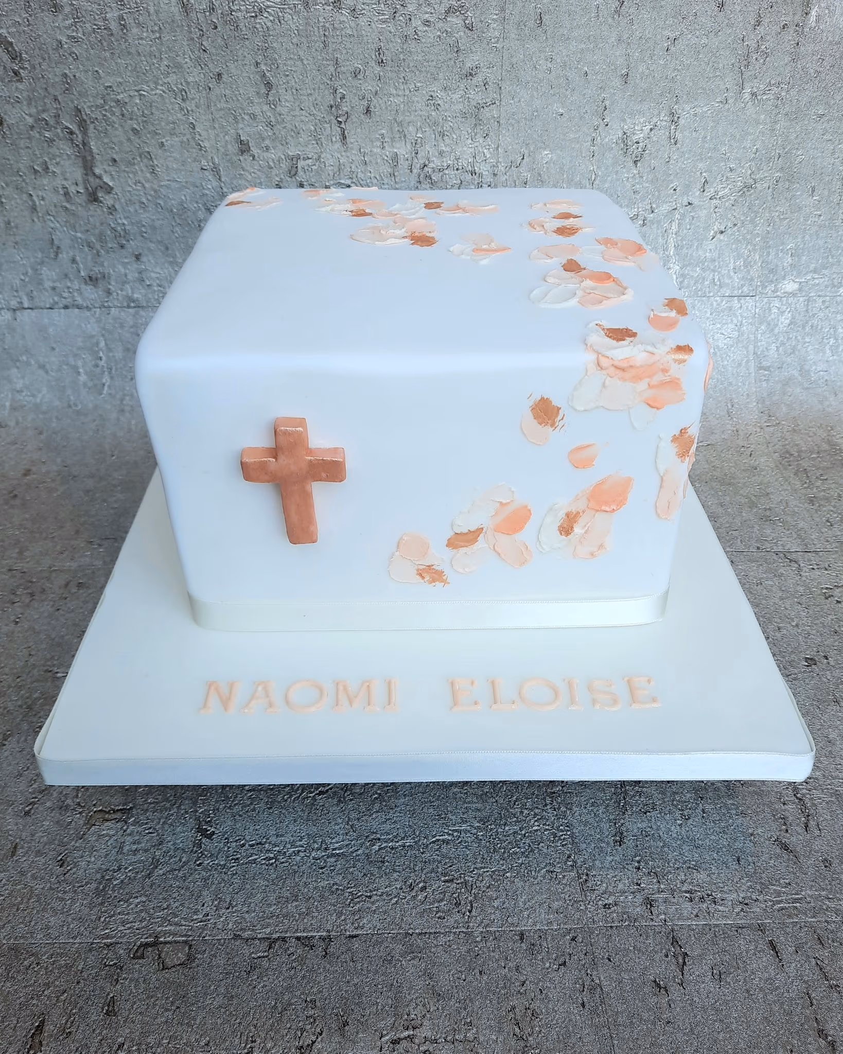 Square white christening cake with rose gold cross and peach brushstrokes