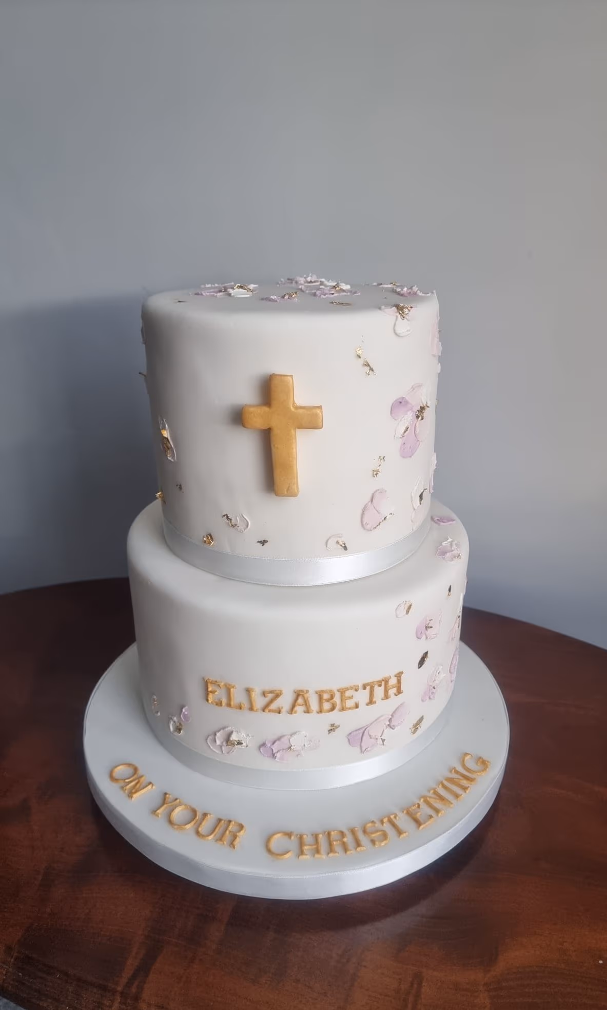 Two-tier white christening cake with gold cross and pink flowers