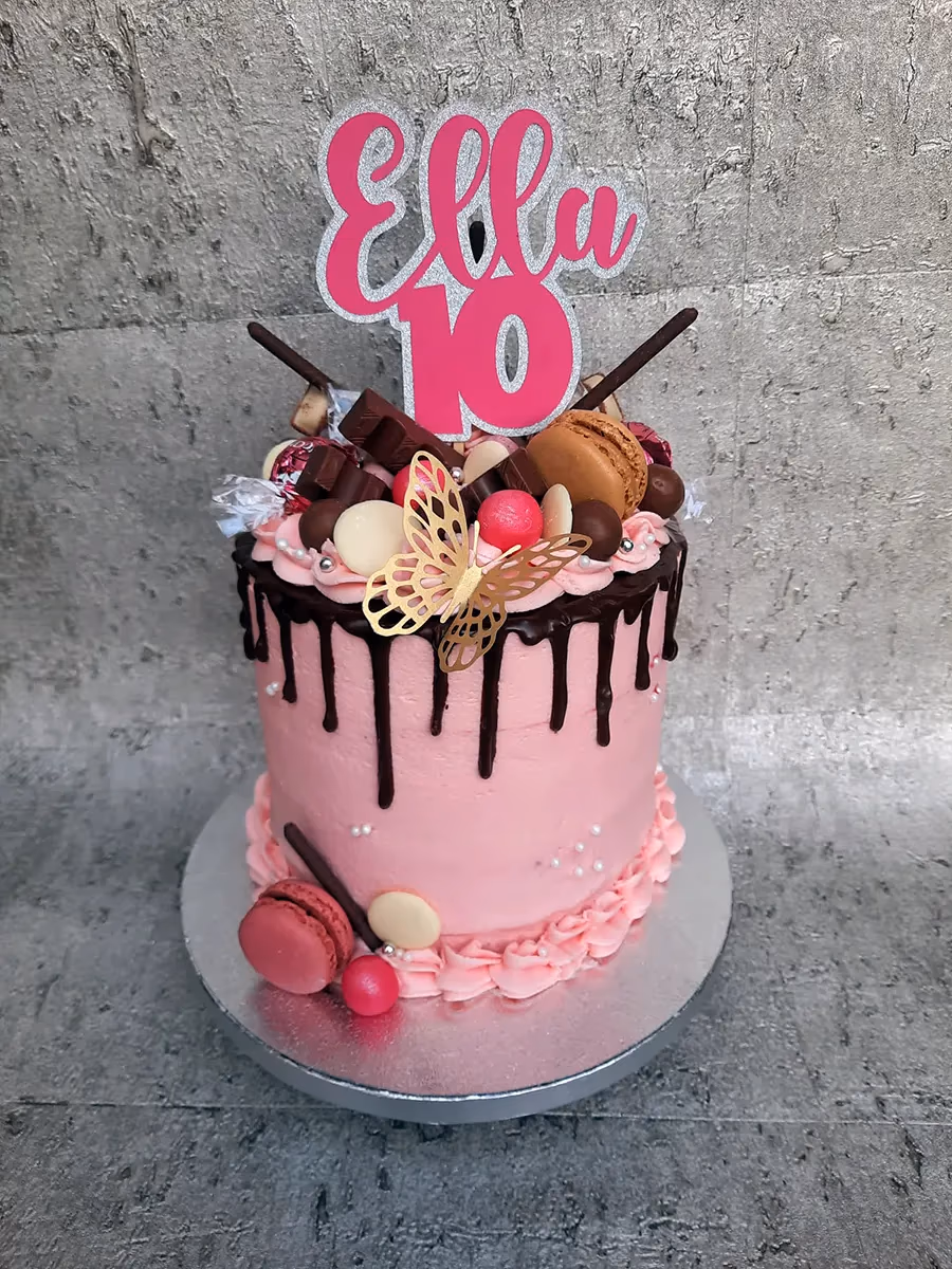 Pink drip cake with chocolate, macarons, and sweets