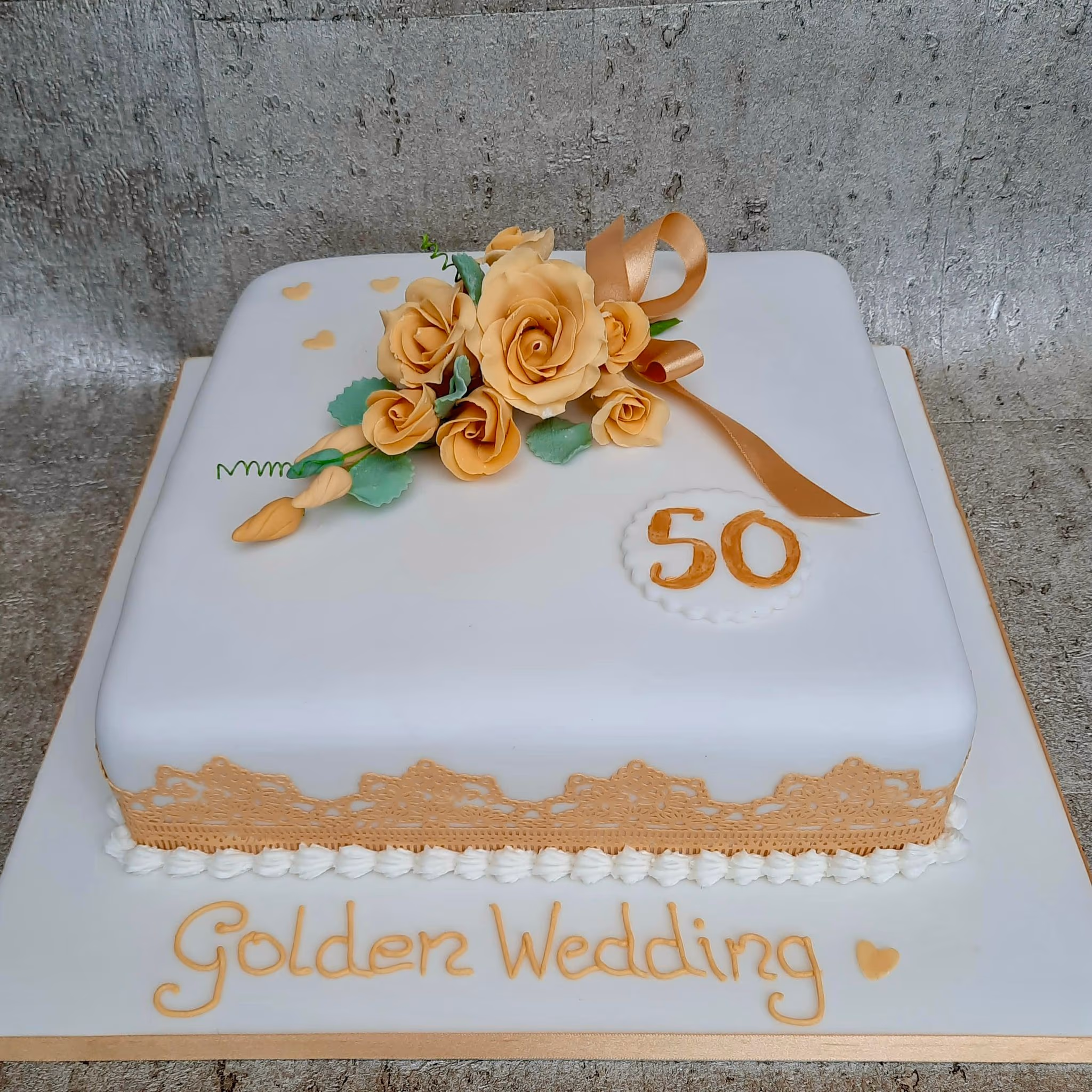 Square golden wedding anniversary cake with white fondant, gold roses and lace