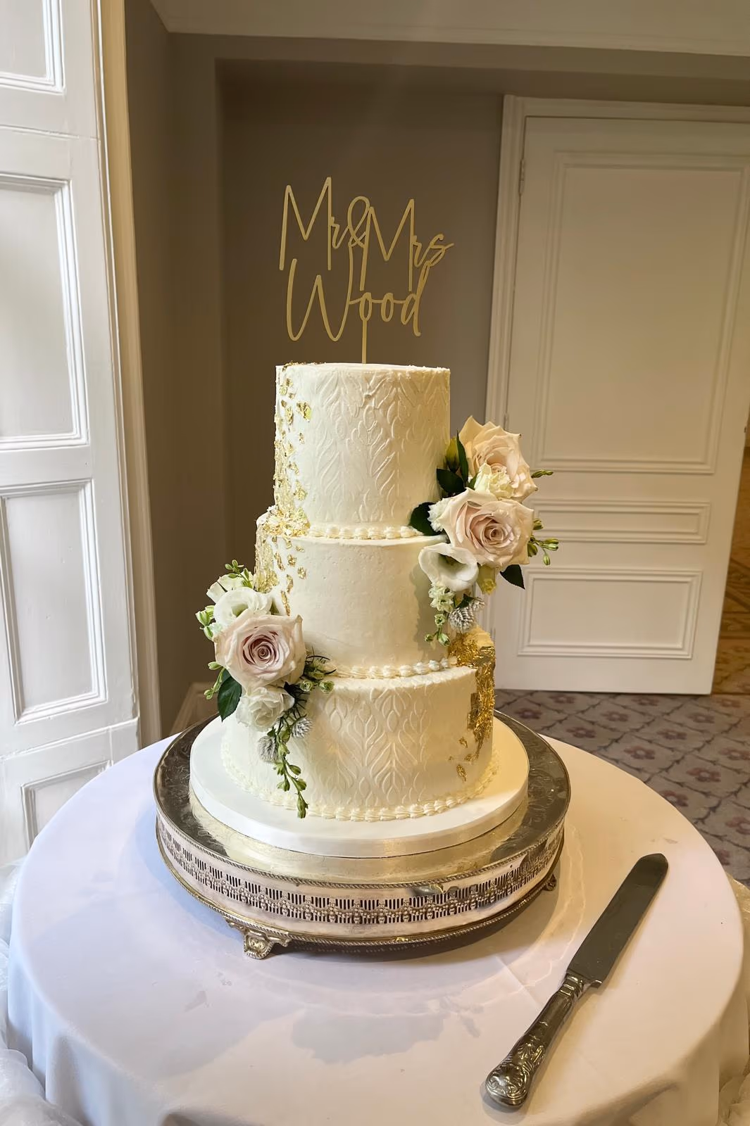 Three-tier cream textured wedding cake with gold leaf and blush white flowers