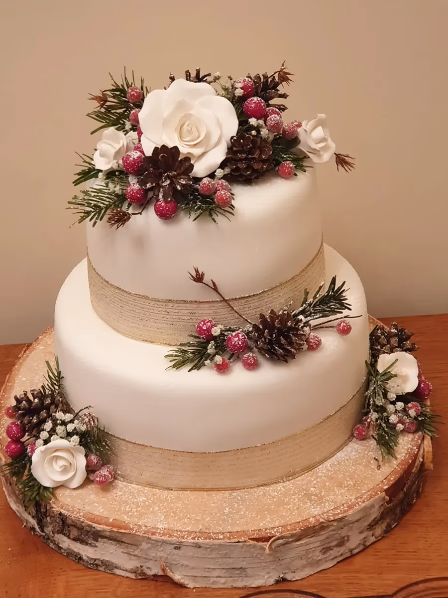 Two-tier winter wedding cake with white fondant, pinecones, berries, and roses