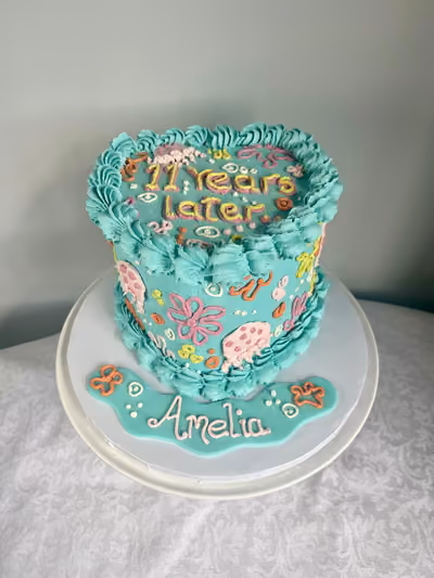 A turquoise vintage-style piped buttercream birthday cake for Amelia reading '11 years later', decorated with piped pastel flowers and swirls.