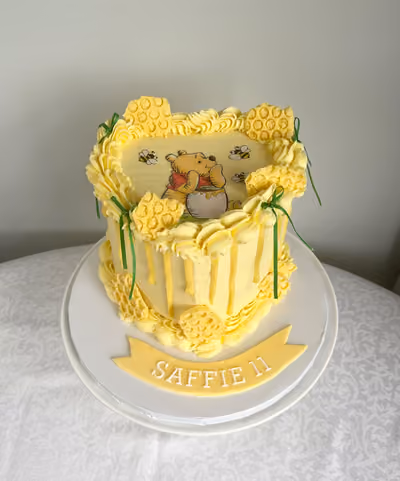 A yellow Winnie the Pooh 11th birthday cake for Saffie with honeycomb decoration, a honey drip, bees and a Pooh picture on top.