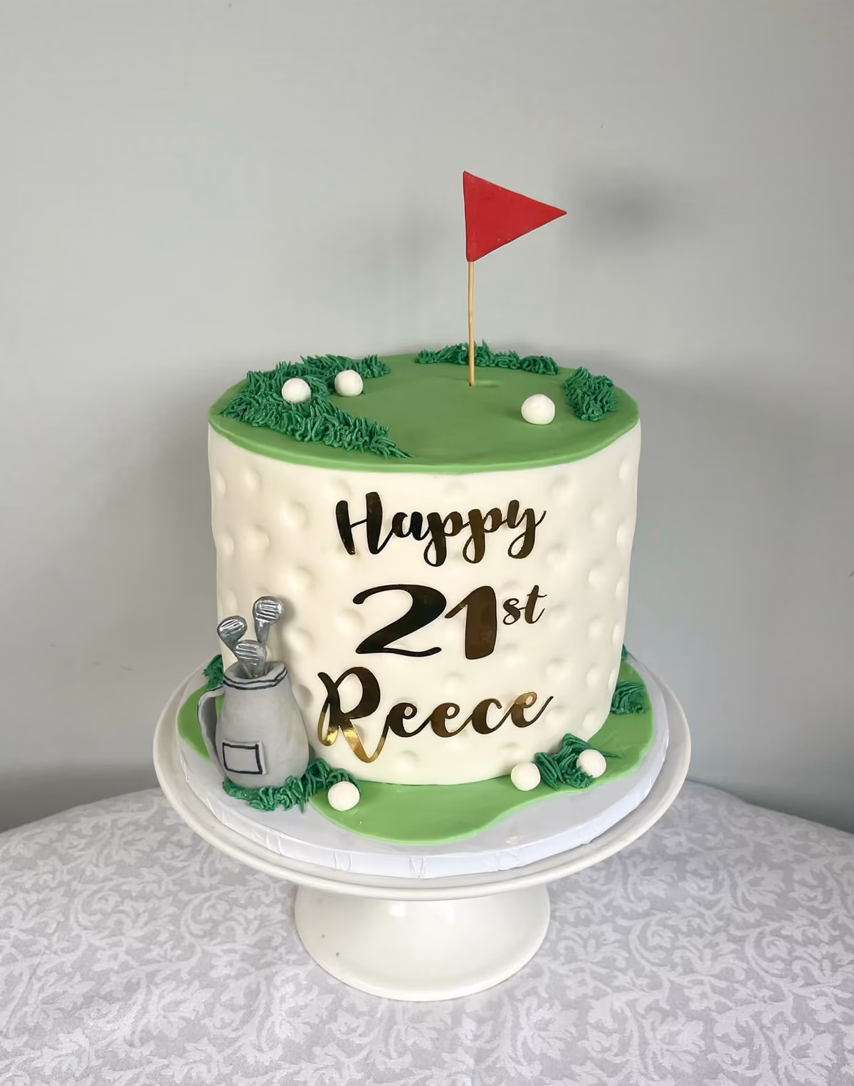 A golf themed 21st birthday cake for Reece, textured like a golf ball, with a green on top holding a red flag and golf balls, and a sugar golf bag at the side.