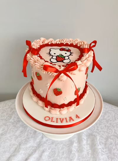A pink vintage-style Hello Kitty 4th birthday cake for Olivia with red piped borders, red satin bows and sugar strawberries.