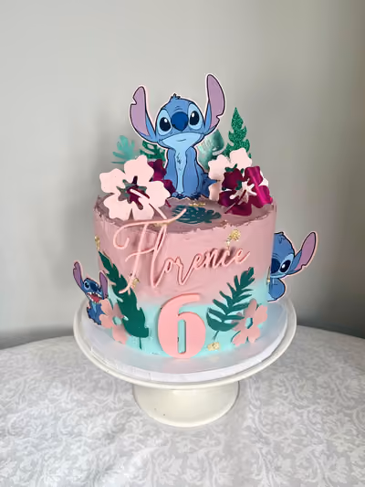 A pink and turquoise Stitch themed 6th birthday cake for Florence with Stitch toppers, pink hibiscus flowers, tropical leaves and a pink '6'.