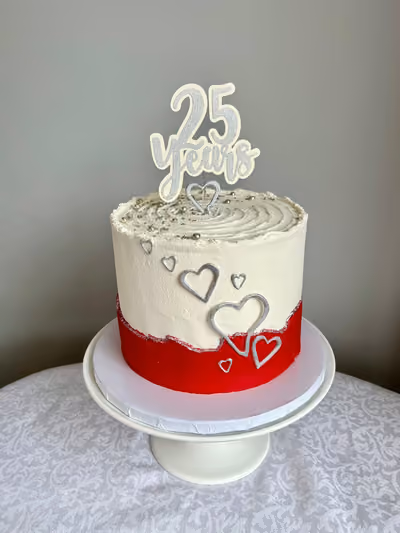 A single-tier anniversary cake celebrating 25 years, with a red bottom half and white top half. It's decorated with silver hearts, silver sprinkles on the white frosting, and a silver glitter '25 Years' cake topper.