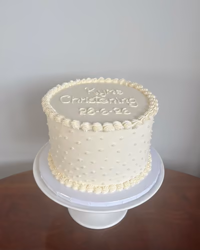 A simple white buttercream christening cake for Kyle with piped dots and borders and 'Kyle Christening' piped on top.