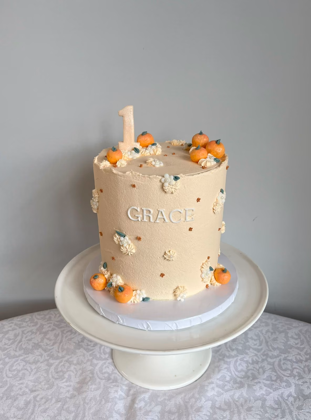 A peach buttercream first birthday cake for Grace decorated with small sugar pumpkins, piped white flowers and a '1' topper.