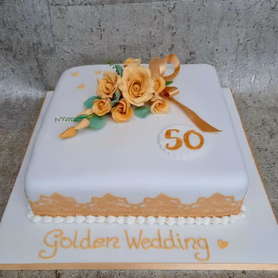 A square white fondant cake for a golden wedding anniversary, decorated with a bouquet of peach and gold roses, a golden ribbon, and the number 50. The cake features a golden lace pattern around its base and the words 'Golden Wedding' in gold script on the board.
