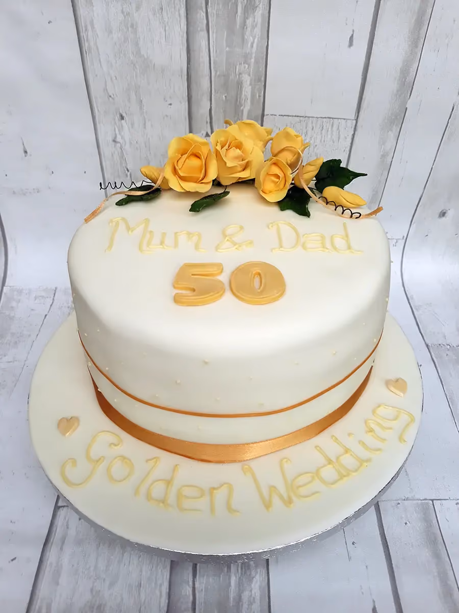 A white single-tier golden wedding anniversary cake decorated with yellow roses, a gold ribbon, and the text 'Mum & Dad 50 Golden Wedding'.