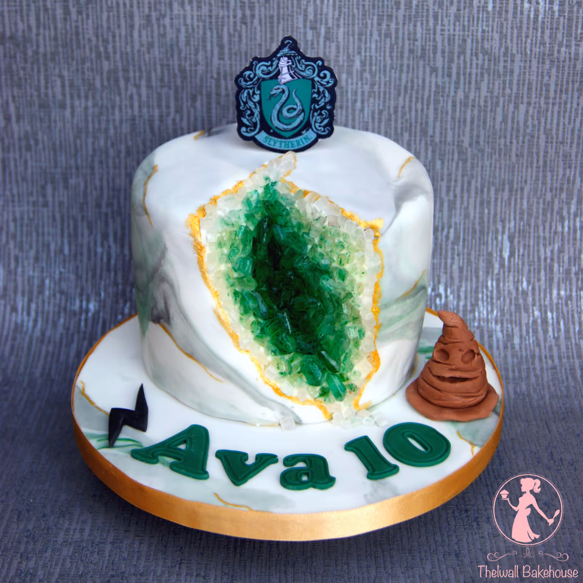 A Harry Potter-themed Slytherin geode birthday cake for Ava's 10th birthday, featuring a white and green marbled cake with an emerald green sugar crystal geode, topped with a Slytherin crest, and decorated on the base with a Sorting Hat, a lightning bolt, and the name 'Ava 10'.