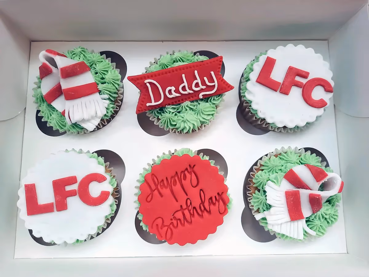 A box of six Liverpool FC themed birthday cupcakes with green frosting, featuring edible decorations like red and white scarves, 'LFC' text, a 'Daddy' banner, and a 'Happy Birthday' message.