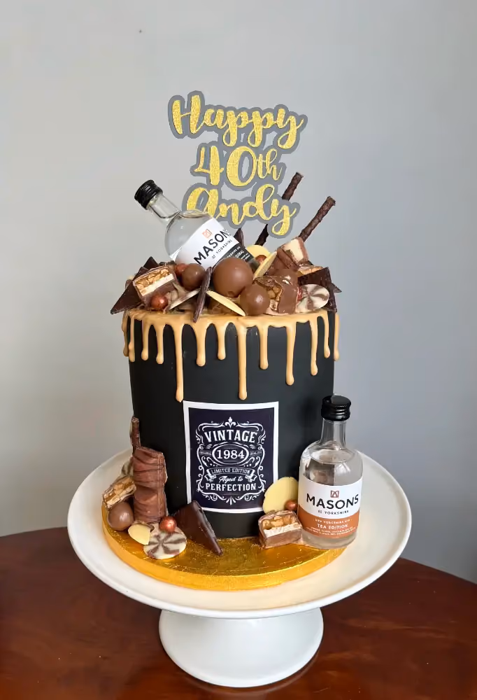 A striking black and gold 40th birthday cake for Andy, adorned with a gold drip, an assortment of chocolates, two miniature Masons of Yorkshire gin bottles, and a 'Happy 40th Andy' topper, with a 'Vintage 1984' label on the side.