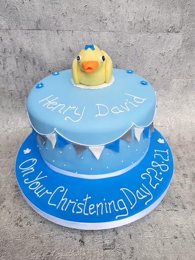 Two-tier blue christening cake with duck topper and bunting